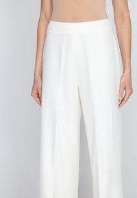 Białe spodnie wide-leg z lekkiego materiału, z płaskim przodem z zakładkami i gładkim pasem. Prezentowane na neutralnym tle.