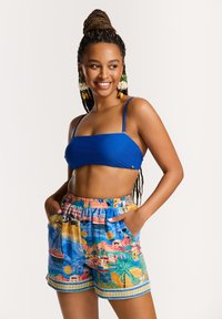 Zils bandeau bikini tops, kas saskaņots ar daudzkrāsainiem īsiem šortiem, kuros attēloti māju, kuģu un palmu skati. Elastīga josta, kabatas.