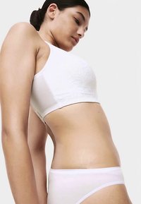 Weißes nahtloses Crop-Top mit Spitzendetails, kombiniert mit passenden weißen Slip. Glatter Stoff und figurbetontes Design, das die Silhouette betont.