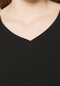 Sort V-hals top lavet af blødt stof, med en glat tekstur og diskrete syninger omkring halsudskæringen og kanterne.