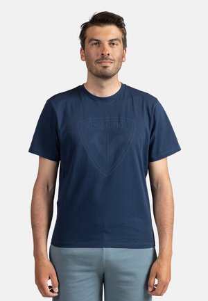 Navy blue cotton t-shirt with a crew neck and short sleeves, featuring a subtle graphic logo in the center. Smooth texture, casual fit.
