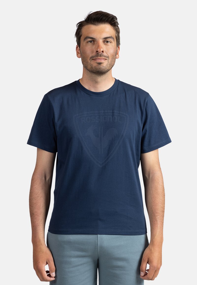 Mørkeblå bomulds T-shirt med rund hals og korte ærmer, prydet med et diskret grafisk logo i midten. Glat tekstur, afslappet pasform.