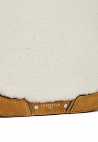 Finta pelliccia color crema con una consistenza morbida, abbinata a accenti in suede beige e hardware argentato, con un'iscrizione del marchio.