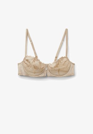 Beżowy biustonosz z fiszbinami i koronką, z regulowanymi ramiączkami oraz małym zawieszonym serduszkiem na środku z przodu.