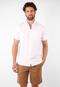 Chemise blanche à manches courtes avec une poche, associ�ée à un short beige. Tissu lisse avec une légère texture, adapté pour une tenue décontractée.