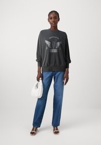 Dark gray sweatshirt with graphic print featuring wings and text, paired with light blue straight-leg jeans and a white quilted handbag.