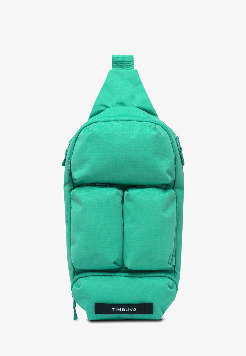 Zaino a spalla verde con quattro tasche frontali imbottite e etichetta nera "TIMBUK2" al centro in basso.