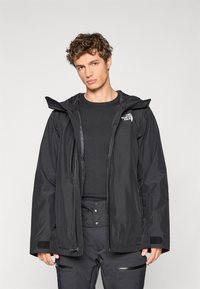 Giacca nera impermeabile realizzata in tessuto resistente, con zip frontale, cappuccio regolabile e polsini in velcro. Abbinate a pantaloni neri.