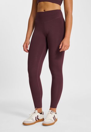 Bordeauxrode actieve leggings met een hoge tailleband, een gladde textuur en minimale naden, gecombineerd met witte sportschoenen met bordeauxrode accenten.