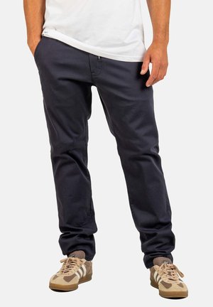 Marineblaue Baumwollhosen mit geradem Schnitt, ausgestattet mit Seitentaschen und einem Reißverschluss, kombiniert mit tan und beigen Sneakern.