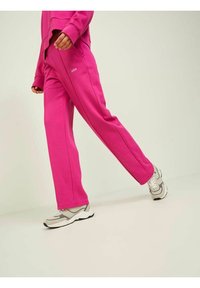 Pantalones de chándal rosas hechos de tela suave, con corte recto y el nombre de la marca "JXXX" en blanco en el muslo izquierdo.