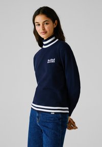 Maglione blu navy con collo alto a righe aderente, dettagli bianchi ai polsini e all'orlo, con il logo Red Bull Racing ricamato sul petto.