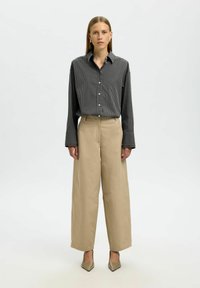 Gestreepte zwart-witte blouse, beige wijde broek en metallic puntige hakken. Soepele stof, ontspannen pasvorm en lange mouwen.