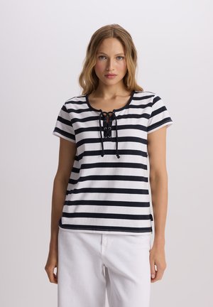 Biała koszulka z poziomymi granatowymi paskami, krótkie rękawy, okrągły dekolt i sznurowany detal z przodu. W zestawie z białymi spodniami.