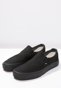 Black canvas slip-on shoes with a rubber sole and elastic side panels for easy wear, featuring a clean, minimalist design.