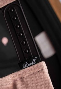 Pink canvas strap with a black plastic adjustment buckle featuring five round knobs and a fabric tag with the brand name "Reell."