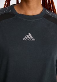 Black athletic t-shirt with short sleeves, crew neck, soft texture, featuring a reflective gray Adidas logo on the front and contrasting shoulder accents.