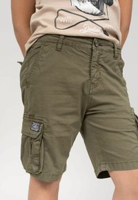 Shorts cargo en coton vert olive, avec une fermeture à bouton, des poches latérales et un logo en patch sur la jambe gauche. Tissu texturé avec des détails de couture.