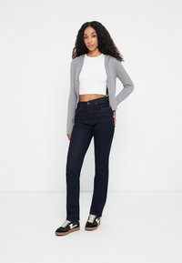 Sweatshirt cinzento com fecho, top cropped justo branco, jeans de pernas retas azul-escuro e sapatilhas pretas com detalhes brancos. Texturas suaves em toda a parte.