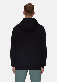 Sweatshirt à capuche noir avec une texture lisse, coupe décontractée et poignets côtelés. Présente des détails discrets du logo au dos. Associé à un pantalon vert clair.