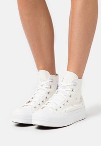 Bílé plátěné vysoké tenisky s fialovými vzory hvězd a měsíce, šněrování, gumové podrážky a polstrovaný kotník.