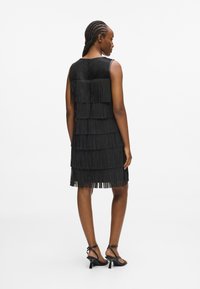 Fekete ujjatlan ruha réteges rojtos díszítéssel, sima textúrával és hátsó záródással. Fekete, pántos magassarkú szandálokkal párosítva.