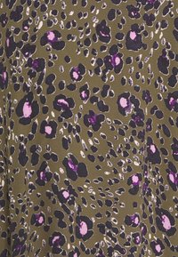 Vihreä kangas, jossa on pilkullinen kuvio ja mustia, valkoisia sekä violetteja leopardin laikkuja. Kudos näyttää pehmeältä ja kevyeltä.