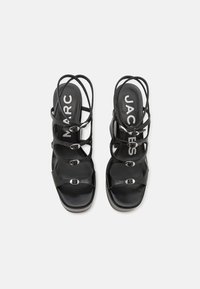 Μαύρες ψηλές σάντες με λουράκια, που διαθέτουν πολλαπλές πόρπες και απαλή υφή. Το λογότυπο εμφανίζεται με προιόν στο εσωτερικό τους.