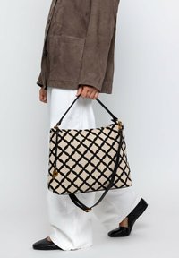 Borsa beige con un motivo geometrico nero, dotata di una tracolla nera e dettagli in oro. Il tessuto appare strutturato e testurizzato.