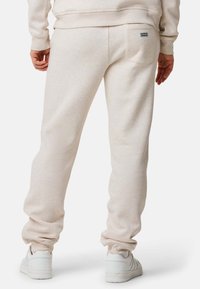 Beiga sweatpants i ett mjukt tyg har en bakficka med en etikett. Mudden är åtsittande vid anklarna och de är i kombination med vita sneakers.