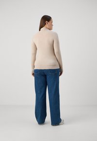 Bežna, prilagojena turtleneck pulover s rebrastim robom, v kombinaciji z širokimi modrimi džinsom. Mehka tekstura, minimalni detajli in nevtralna barvna paleta.