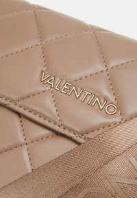 Beige steppelt bőrtáska arany "Valentino" logóval, sima felülettel és mintás díszítéssel rendelkező vízszintes pánttal.