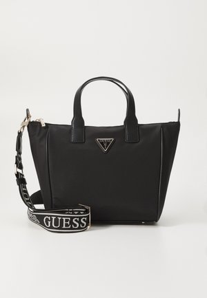 Czarna torba typu tote marki Guess z skórzanymi rączkami, trójkątnym metalowym logo oraz odpinanym, materiałowym paskiem na ramię z logo, na jednolitym tle.