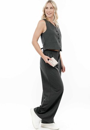 Gray cropped vest with buttons, paired with loose gray trousers and white sneakers. Model holds a textured wallet.