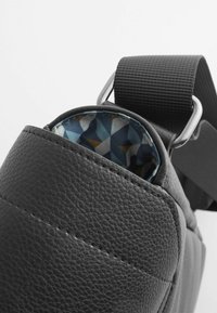 Black leather bag with textured exterior, showing a patterned blue and geometric interior lining, and a sturdy black strap with metal hardware.