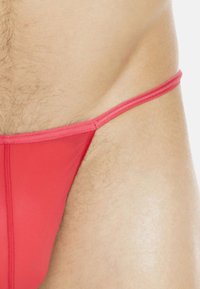 Rote thong Badebekleidung aus einem glatten, dehnbaren Material mit minimalistischem Design und dünnen Trägern, die einen enganliegenden Schnitt präsentieren.