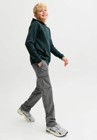 Tamnozeleni dukserica s kengurskom džepom, uparena sa sivim cargo hlačama s bočnim džepovima. Sivi tenisica s teksturiranom površinom.