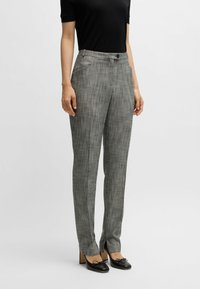 Harmaat ruutuhousut, joissa on slim fit -leikkaus, napin sulkeminen, sivutaskut ja sileä pinta. Yhdistetty mustiin korkokenkiin.