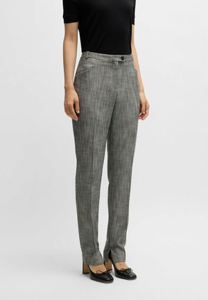 Graue karierte Hosen mit taillierter Passform, die einen Knopfverschluss, Seitentaschen und eine glatte Textur aufweisen. Kombiniert mit schwarzen High Heels.