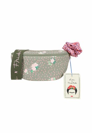 Sac banane floral vert avec motif à pois rose, sangle verte avec texte blanc, fleur en tissu rose et une étiquette Frida Kahlo attachée.
