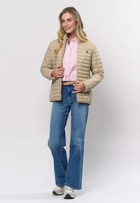 Bēšs pūkains mētelis ar kvadrātveida rakstu, rāvējslēdzēju priekšpusē un logo. Valkāts virs rozā krekla un kopā ar ziliem paplašinātiem džinsiem un pelēkām sporta kurpēm.