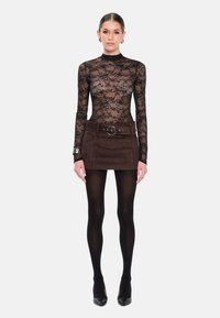 Zwarte kanten langamige bodysuit, gecombineerd met een bruine suède mini-jurk met een riem met een grote ronde gesp, gedragen met zwarte panty’s en hakken.