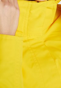 Zbliżenie na rękę trzymającą kołnierz jasnoniebieskiej kurtki z widocznymi detalami szycia.