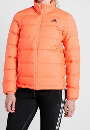 Personne portant une veste matelassée Adidas orange vif avec une fermeture éclair à l'avant et des leggings noirs avec des bandes blanches.