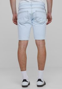 Shorts de mezclilla azul claro con un corte limpio, que cuentan con dos bolsillos traseros y costuras visibles. Combinados con calcetines blancos y zapatos con acentos negros.