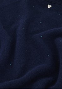 Donkerblauwe trui van zachte stof, met kleine sprankelende pailletten en een hartvormige halslijnaccent. Gladde textuur.