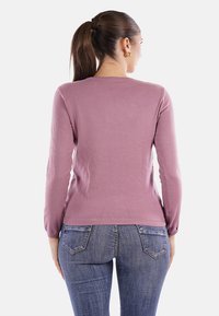 Pullover a maniche lunghe in morbido tessuto malva, taglio aderente, con polsini e orlo a coste, abbinato a jeans blue denim con tasche posteriori.