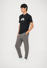 Schwarzes Baumwoll-T-Shirt mit einem weißen Grafikdesign, kombiniert mit grauen tapering Jogginghosen und weißen Sneakers mit strukturiertem Finish.