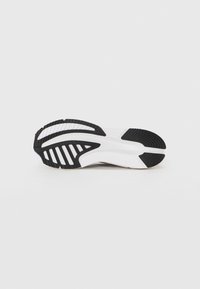 Semelle de chaussure avec une couche extérieure en caoutchouc noir à motifs texturés, une section médiane blanche et un dessin de bande de roulement distinct pour une meilleure traction.