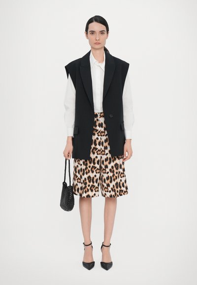 Black tailored vest over a white shirt, paired with leopard-print shorts. Accessories include a small black handbag and pointed heels.